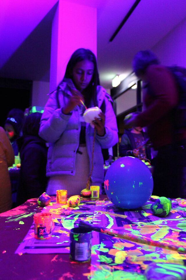 A girl paints a rock with luminous paint, surrounded by purple light